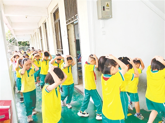 演練中，學(xué)生雙手抱頭、緊貼墻角，按照指定的逃生路線快速有序地撤離至操場安全區(qū)域。